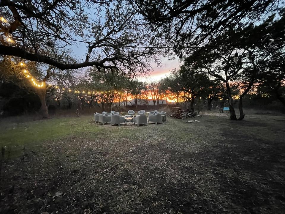 A ring of chairs in an oak grove with string lights at sunset